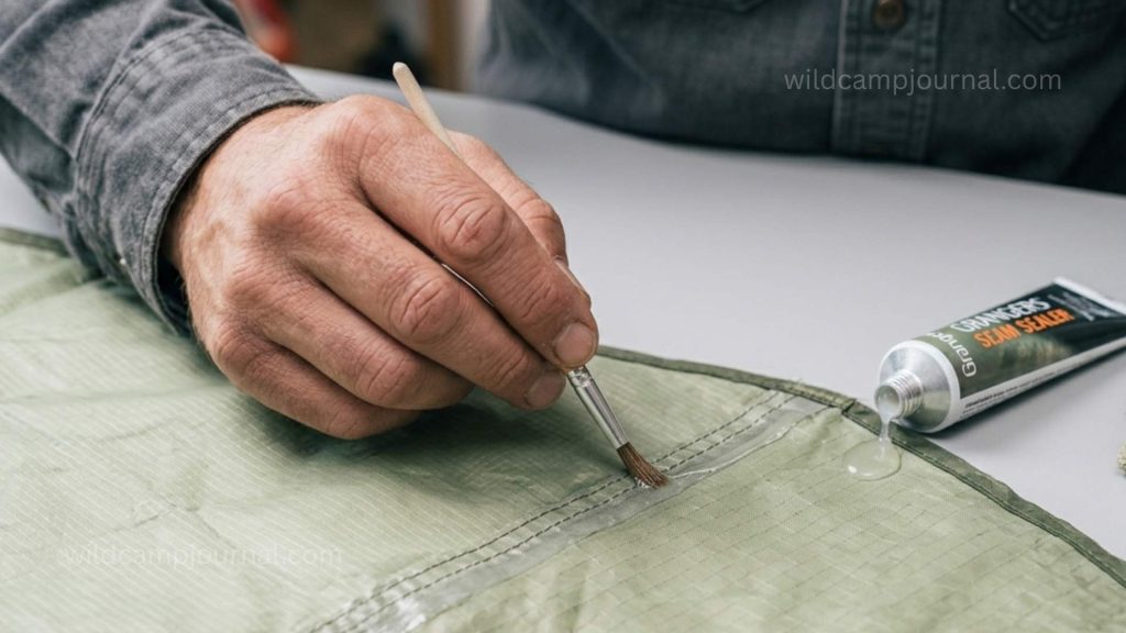 Close-up of hand applying seam sealer with a small brush along a tent seam stitching line on a rainfly laid flat and turned inside out