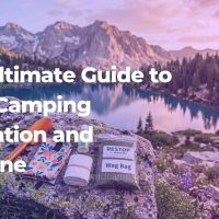 A complete wild camping sanitation kit featuring an ultralight trowel, hand sanitizer, and WAG bag laid out on a rock overlooking a mountain lake.